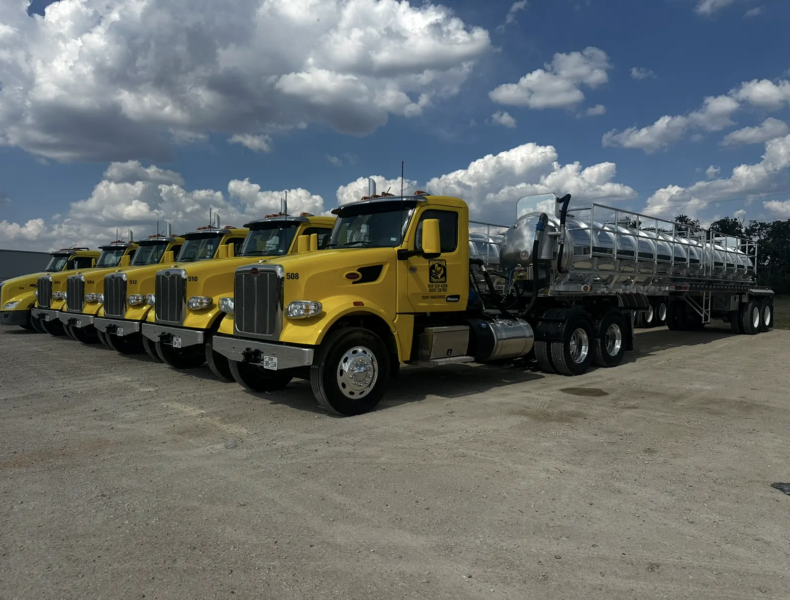A row of yellow Wrangler tractors with steel tank trailers